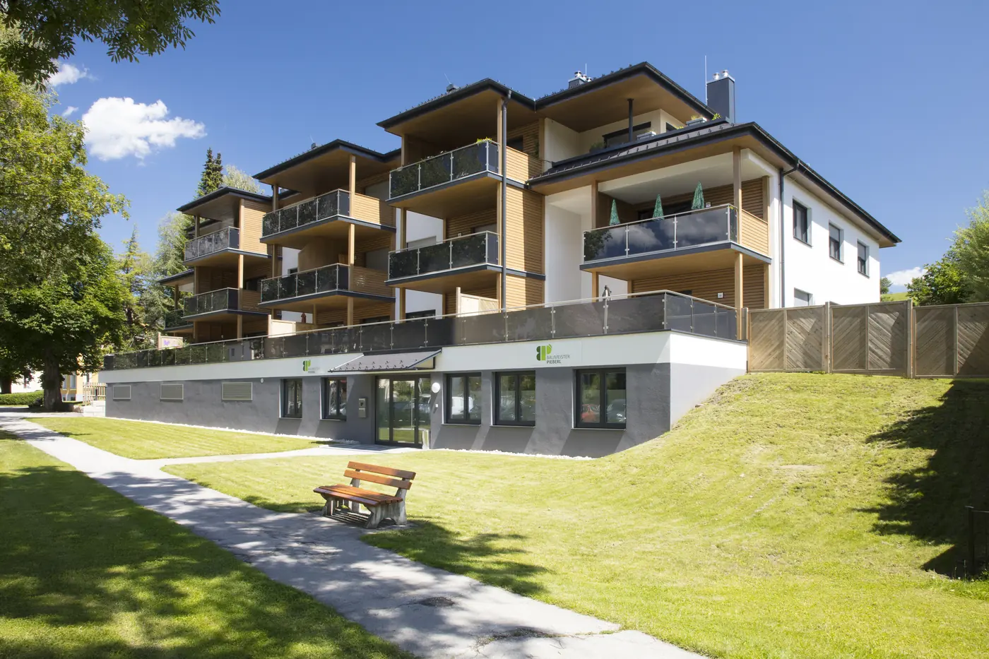 Moderne Wohnanlage mit Holzbalkonen und Grünfläche an einem Sommertag